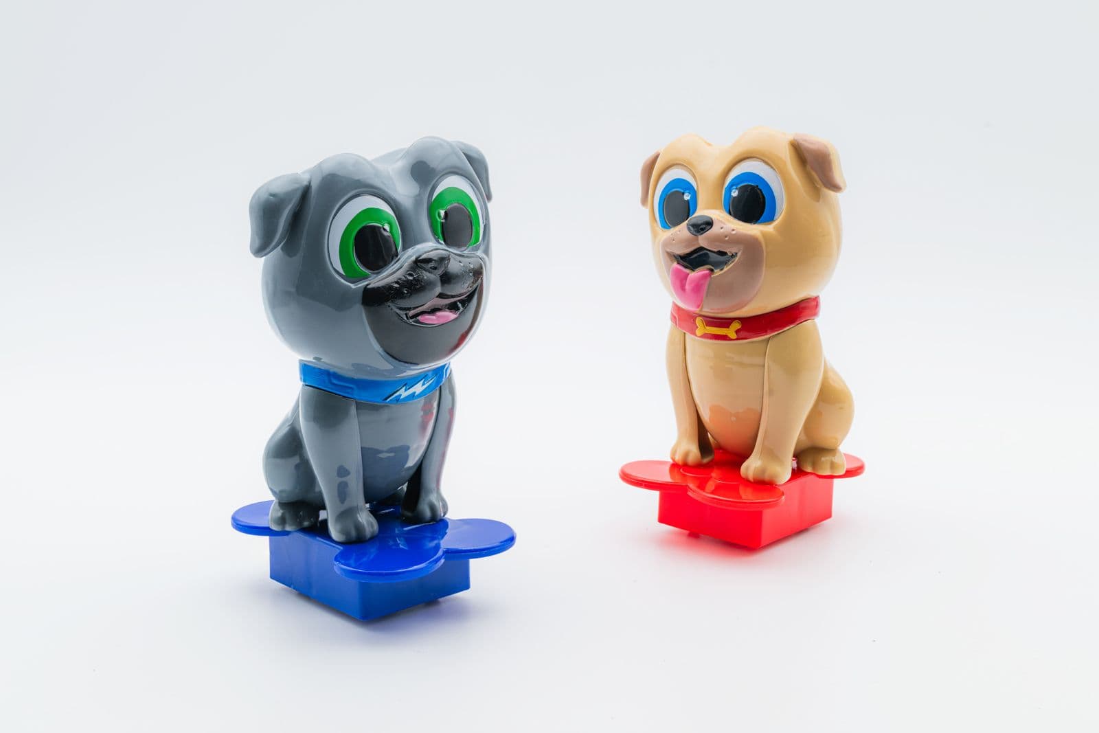 Glossy character figures of Bingo and Rolly from Puppy Dog Pals, seated on blue and red paw-shaped bases against a white background.