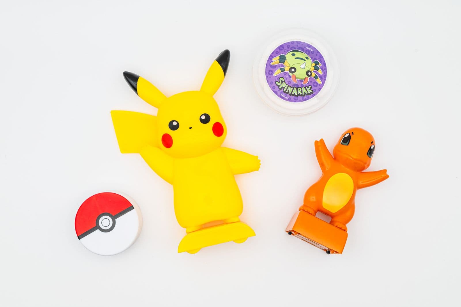 Colourful Pokémon products featuring Pikachu and Charmander character pieces, a round Poké Ball design and a clear container with Spinarak artwork.